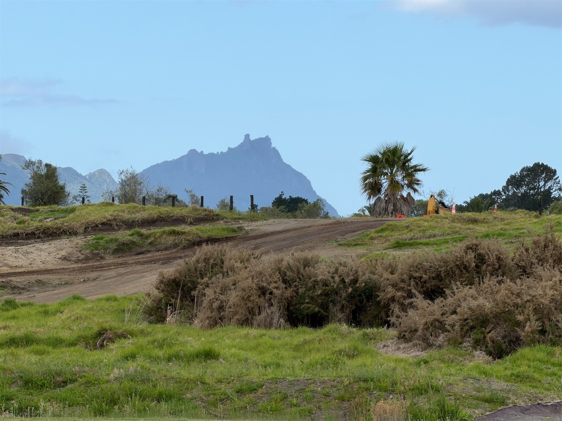 A hill with a jagged top in the distance behind grass and earthworks.