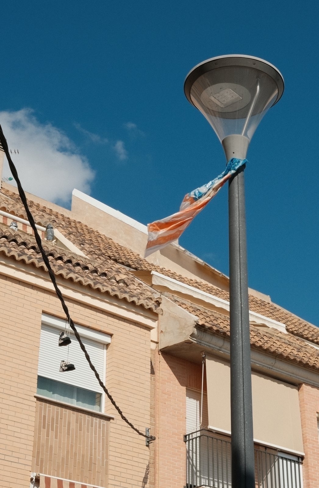 Auto-generated description: A flag is caught on a streetlight in front of a building with a clear blue sky overhead.