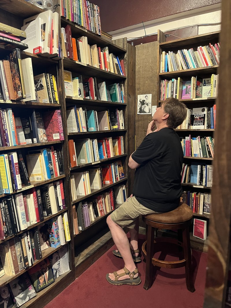 Justin perched on a stool studying the shelves in an Ashland used bookstore