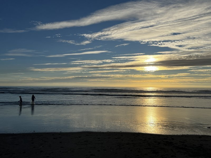 Two figures at the water's edge as the sun drops toward the horizon
