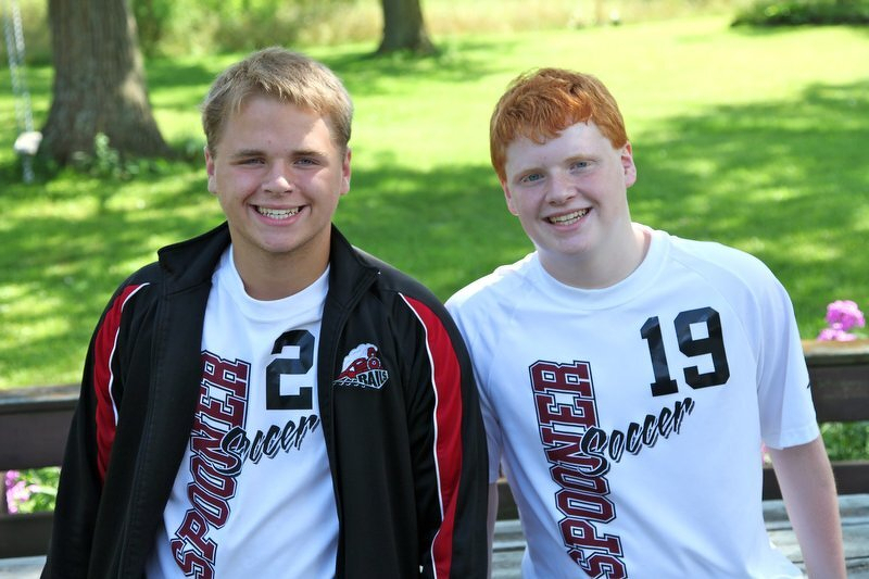 Two teammates in soccer jerseys, numbers 2 and 19, grinning outside on a summer day
