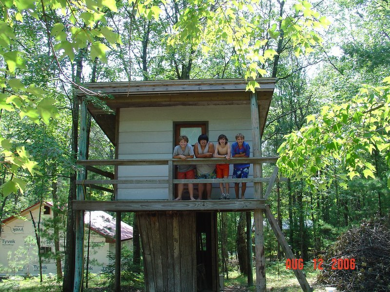 The treehouse up in the trees with the kids leaning over the porch railing