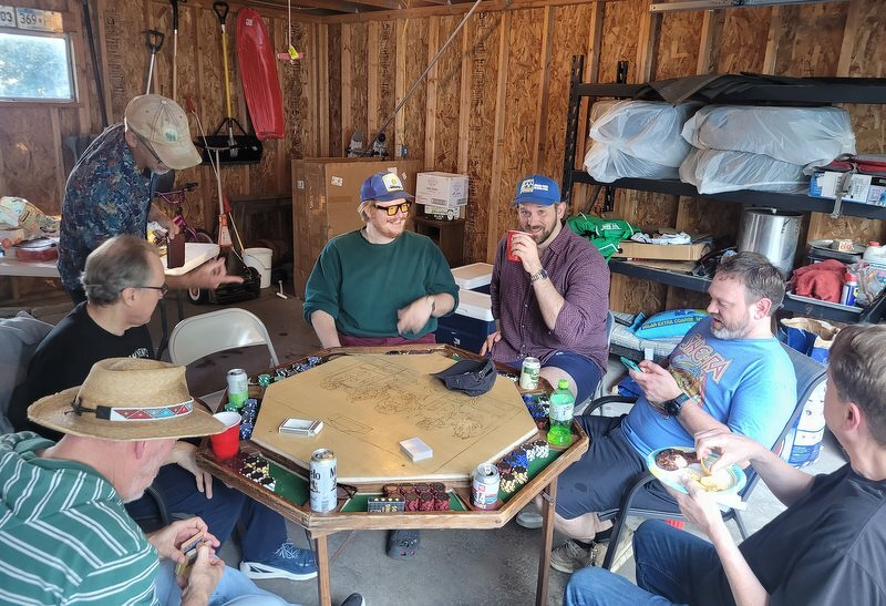 Seven players around the octagonal poker table in Robert's garage, cards and cans and chips spread across the felt