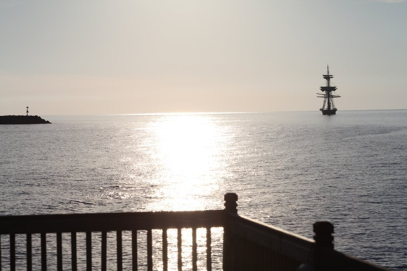 A tall ship anchored offshore at sunrise, seen past the deck railing