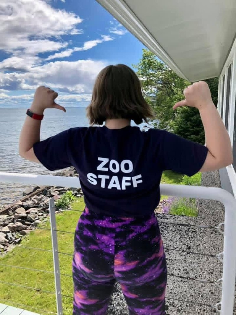 Kaylee on the deck above Lake Superior, thumbs pointed back at the ZOO STAFF lettering on her shirt