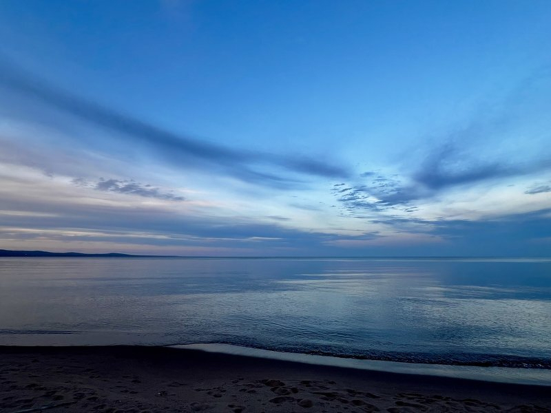 Blue dusk over Lake Superior, with soft clouds reflected in the calm water at the beach