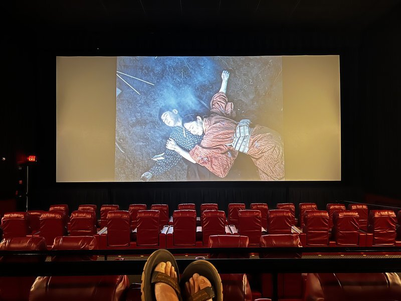 An empty movie theater with rows of red seats, my feet propped up as the previews play on the big screen