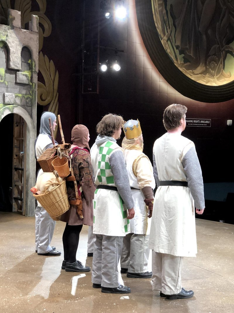 The Spamalot cast in costume gathered on stage under the lights during the promo video shoot