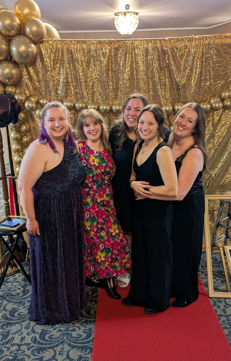 Kaylee and the rest of the creative team in evening gowns posing on the red carpet in front of a gold sequin backdrop and balloons on opening night of A Chorus Line