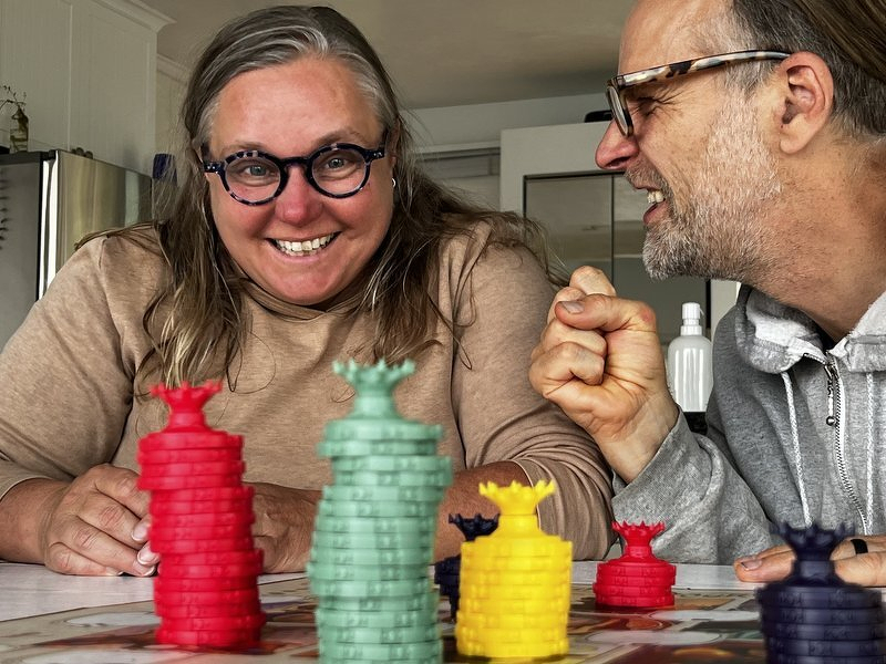 Brandy and Tom laughing across the table behind stacks of colorful Cursed Court chips