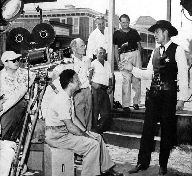 A black and white photo of Fred Zinnemann and crew beside the camera on the set of High Noon, with Gary Cooper in his marshal's costume