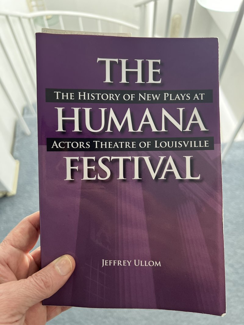 Holding up a copy of The Humana Festival: The History of New Plays at Actors Theatre of Louisville by Jeffrey Ullom