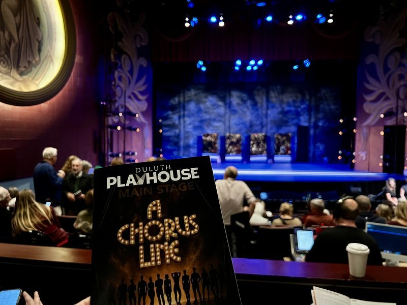 Holding up the Duluth Playhouse program for A Chorus Line in front of the blue-lit NorShor stage before the show