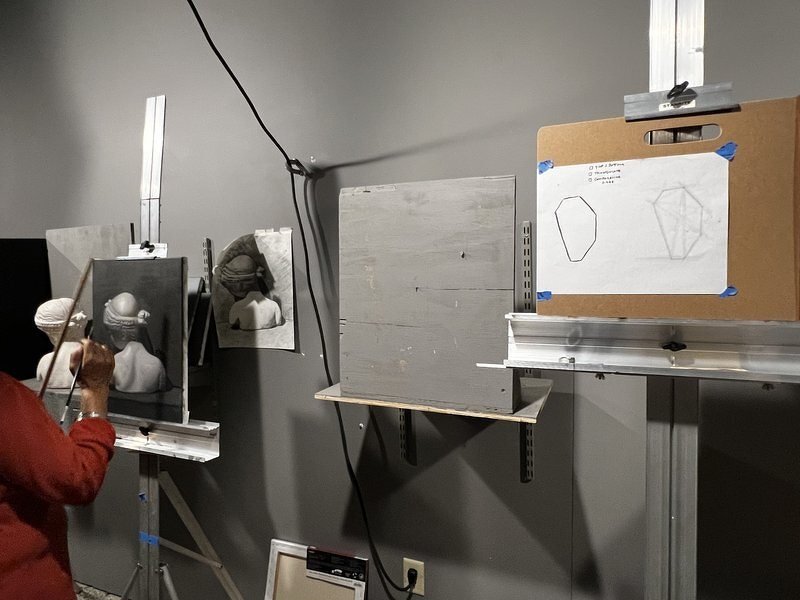 My easel with a few tentative pencil lines on white paper, next to a classmate painting a beautifully rendered plaster cast bust