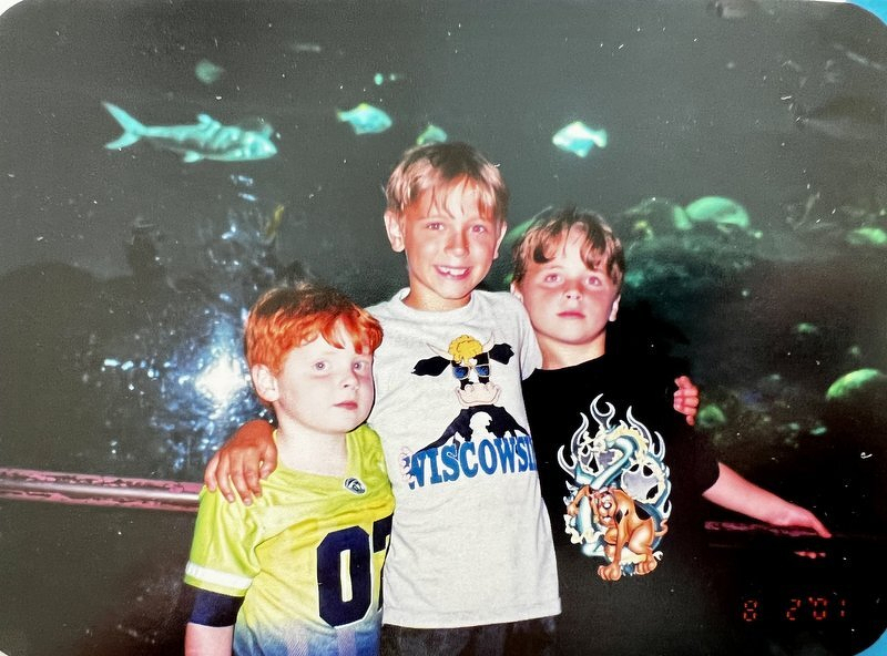 Alex, Corey, and Spencer posing in front of a glowing aquarium tank full of fish