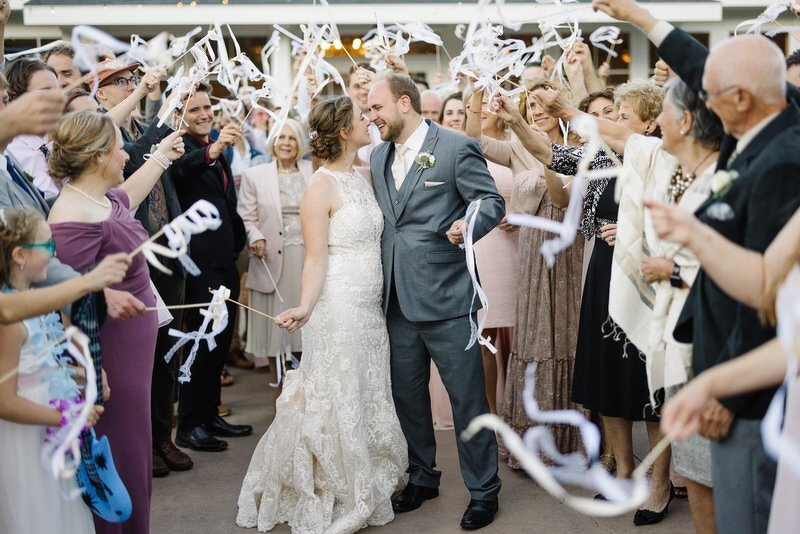 Alex and Kelsie leaving their wedding through a tunnel of streamers and cheering guests