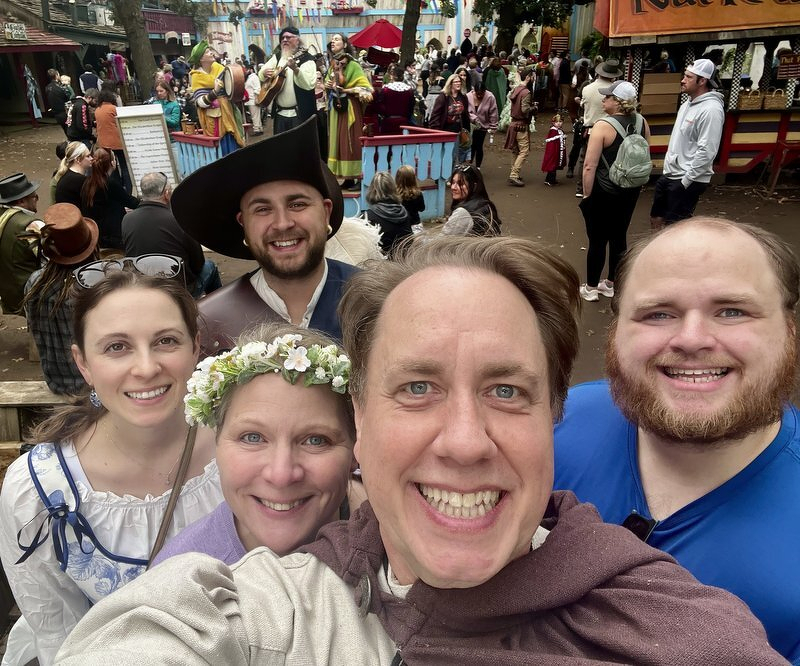 A selfie of the five of us in costume in the middle of the festival lane, one in a flower crown and one in a fancy hat