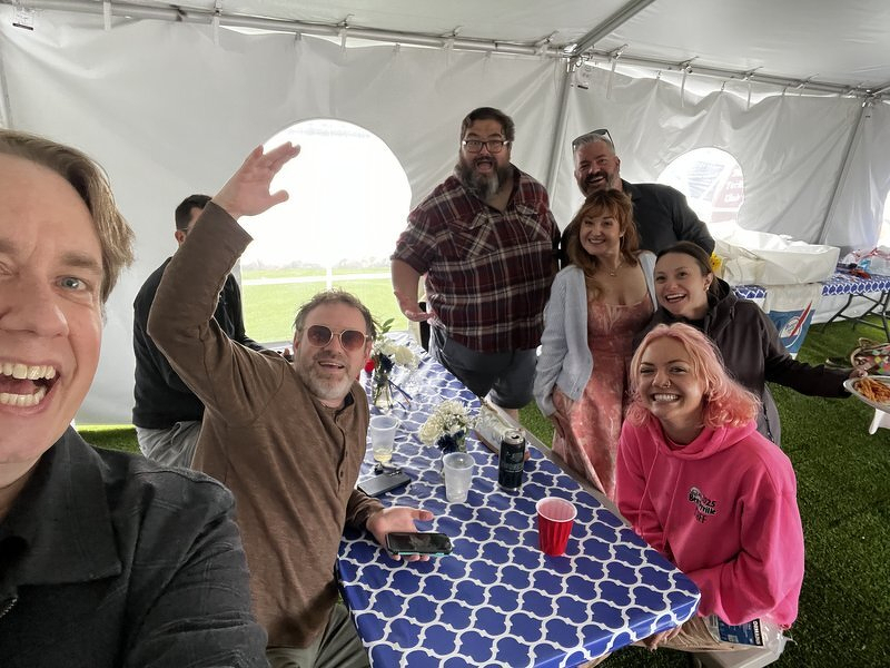 Friends around the reception table, one of them waving at the camera