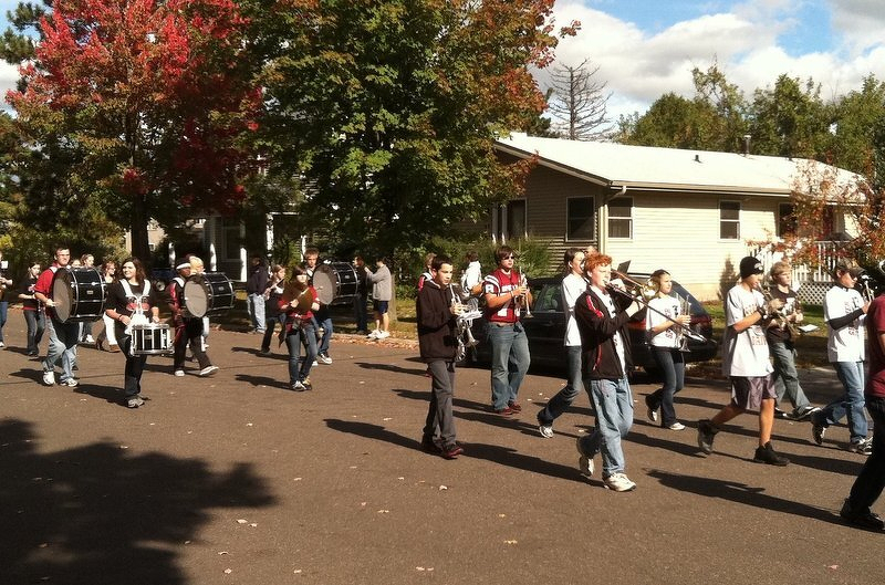The middle school marching band coming down the street in the 2011 homecoming parade, trombones out front and red maples overhead