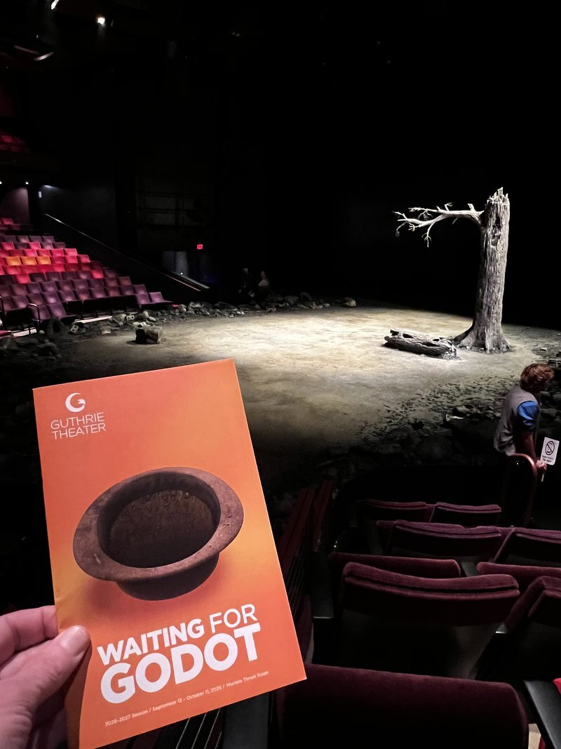 The orange Waiting for Godot program held up in front of the Guthrie stage, a bare tree in a pool of light