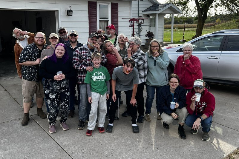 A big group photo of the extended family gathered in front of the farmhouse garage and eating cookies
