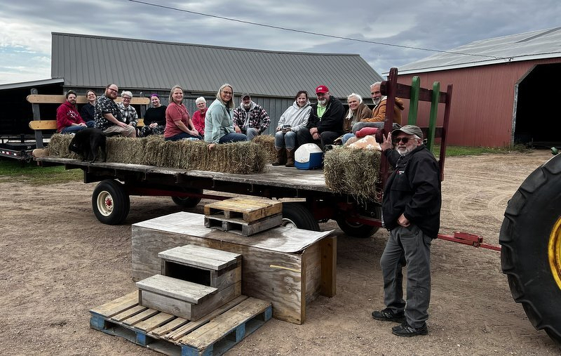 Family members sitting on hay bales on a flatbed wagon, ready for the hay ride, with the tractor and barn behind them