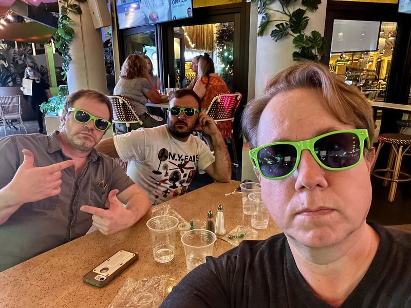 Robert, Daniel, and Justin in matching green sunglasses at a restaurant table