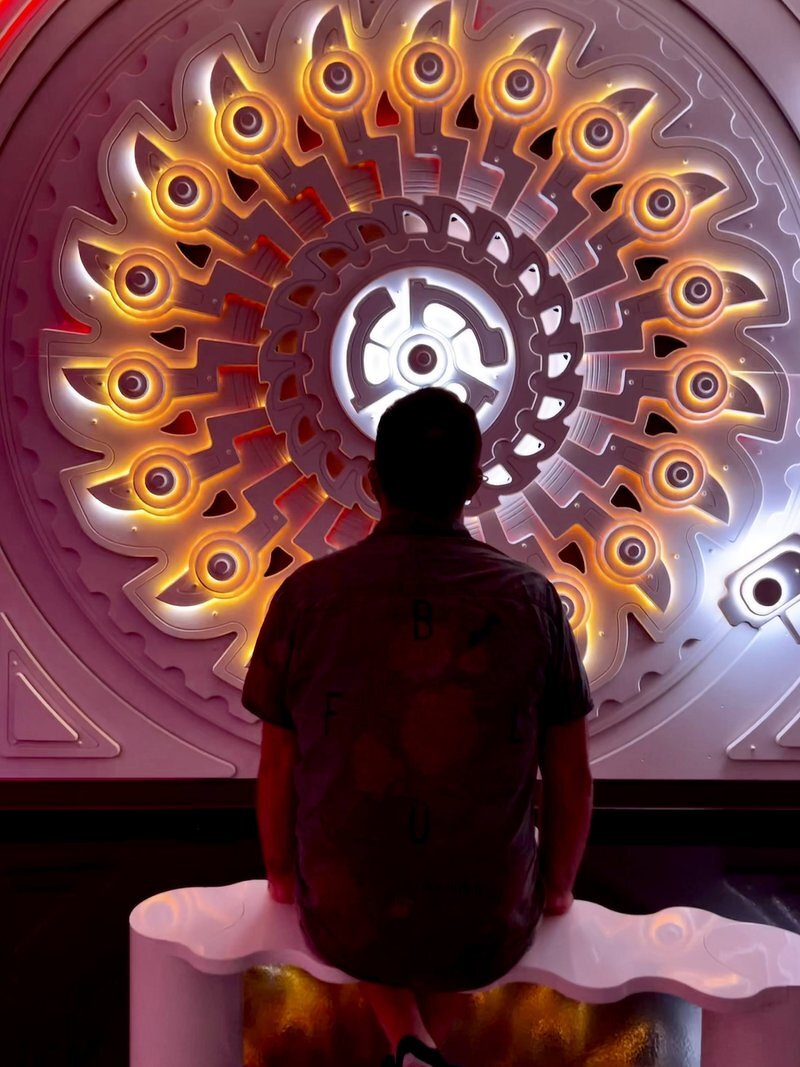 Daniel seated before a huge glowing mandala of lights and eyeballs