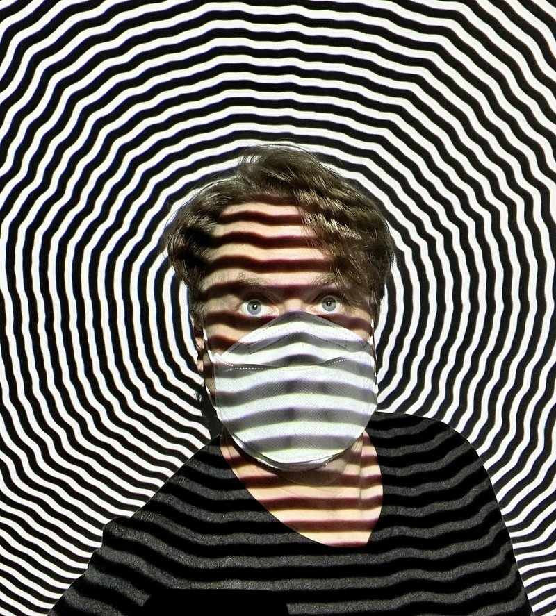 Justin in a mask against a dizzying black-and-white concentric wave pattern projected across his face