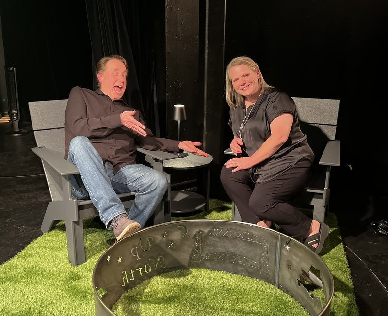 Justin and Jody lounging in a pair of gray Loll chairs on a patch of artificial turf beside a metal fire ring
