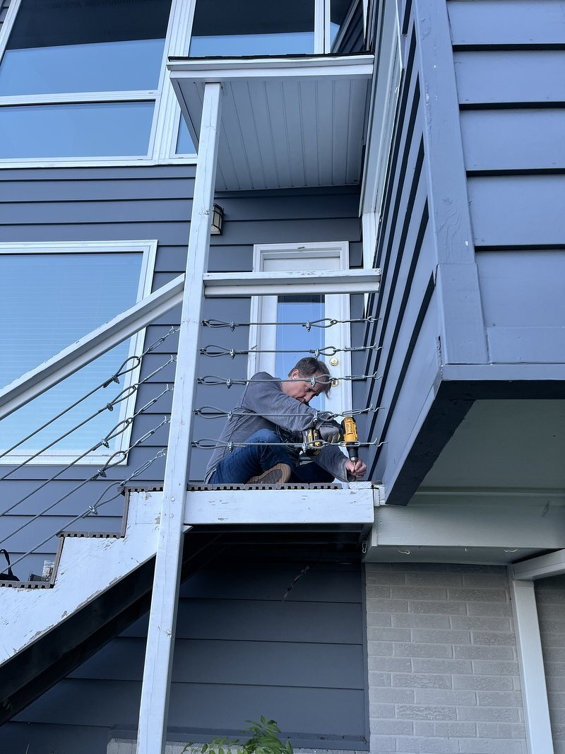 Justin with a drill, working on the top platform of the exterior stairs on the side of the house