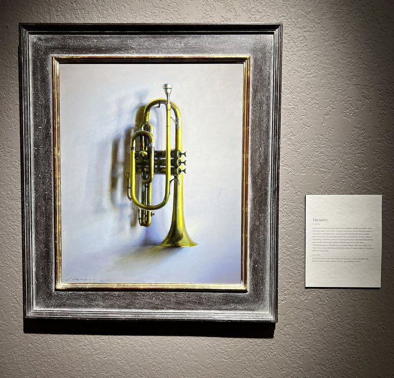 A Jeffrey Larson painting of a brass trumpet hanging against a pale wall