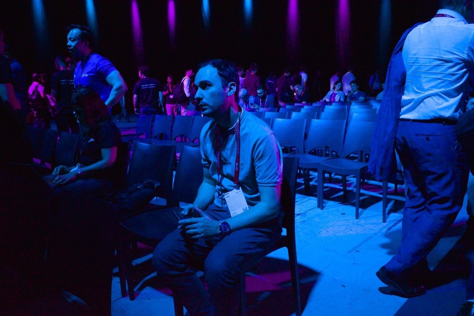 People are seated and standing in a dimly lit auditorium with blue and purple lighting.
