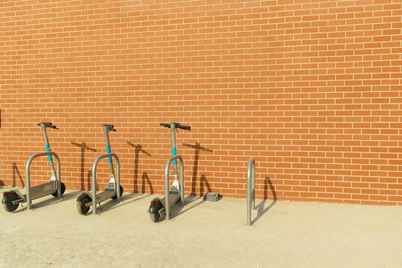 Three scooters are parked in stands against a brick wall.
