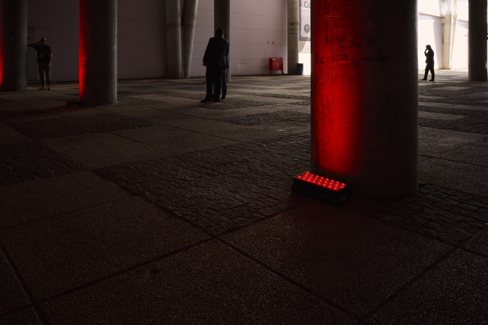 Several individuals stand in a dimly lit space with red lights illuminating concrete pillars.