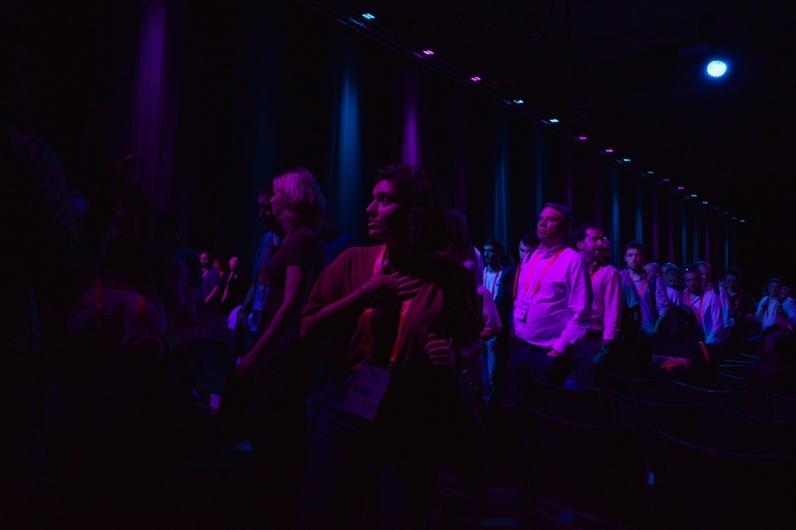 A group of people is gathered in a dimly lit room, illuminated by a purple light, creating a dramatic atmosphere.
