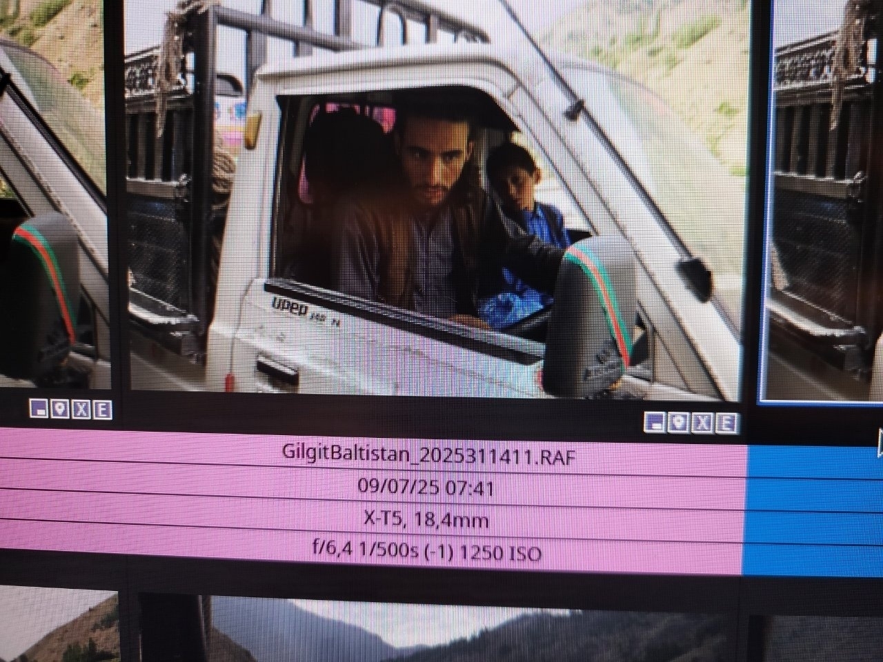 A man and a child are sitting inside a vehicle, with mountainous scenery visible outside.