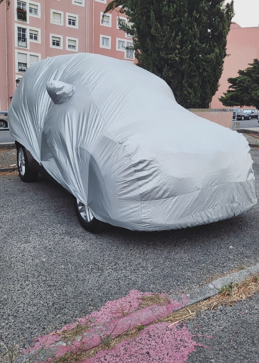 A car is parked outside with a protective cover draped over it.