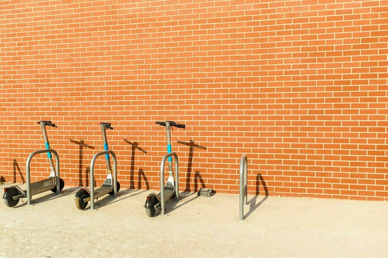 Three electric scooters are parked beside a brick wall on a sunny day.