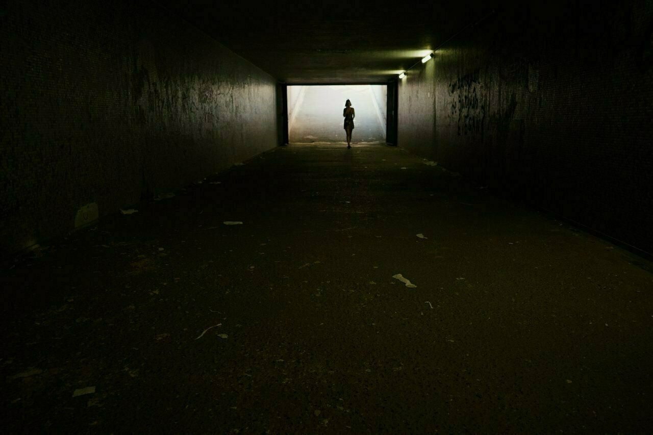 A person is silhouetted against light at the end of a dark tunnel.