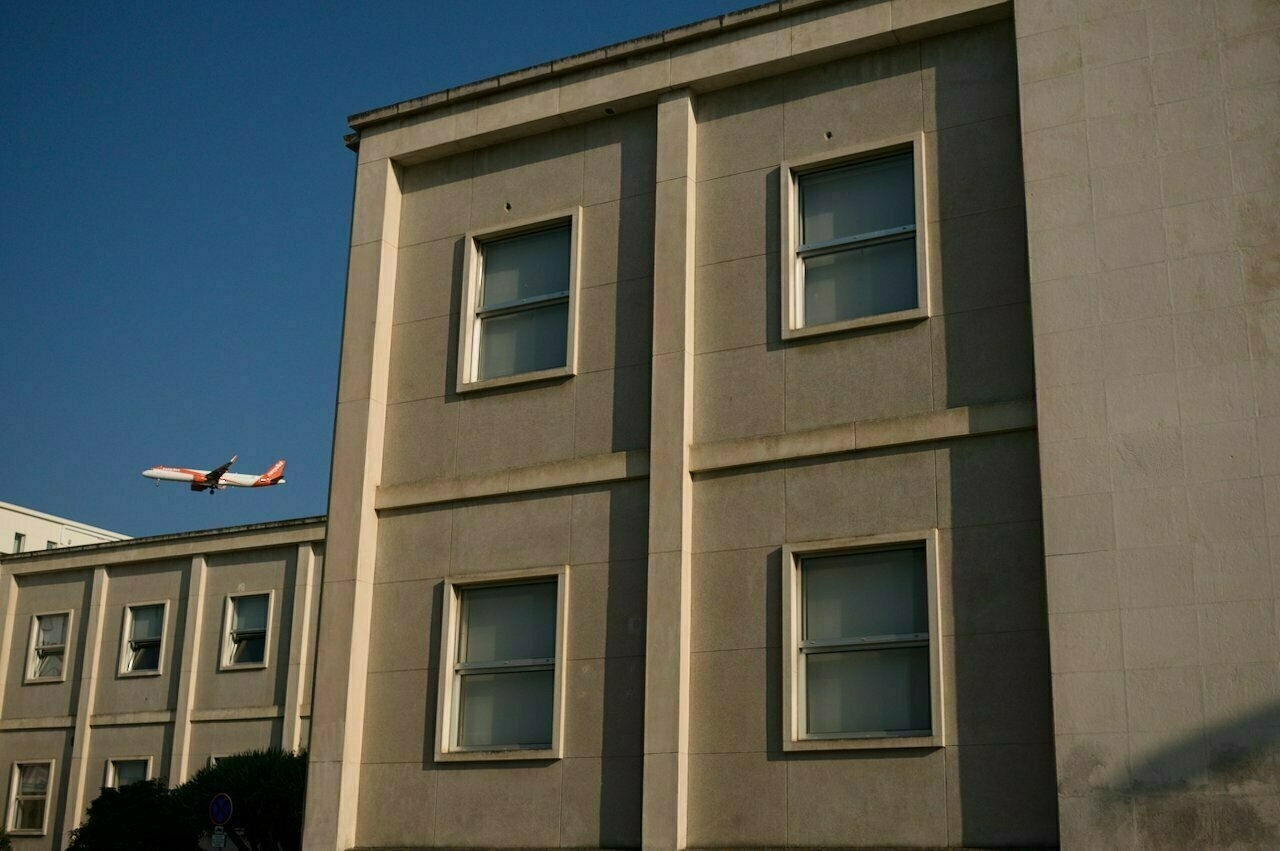 A small aircraft is flying in the sky near a large building with multiple windows.