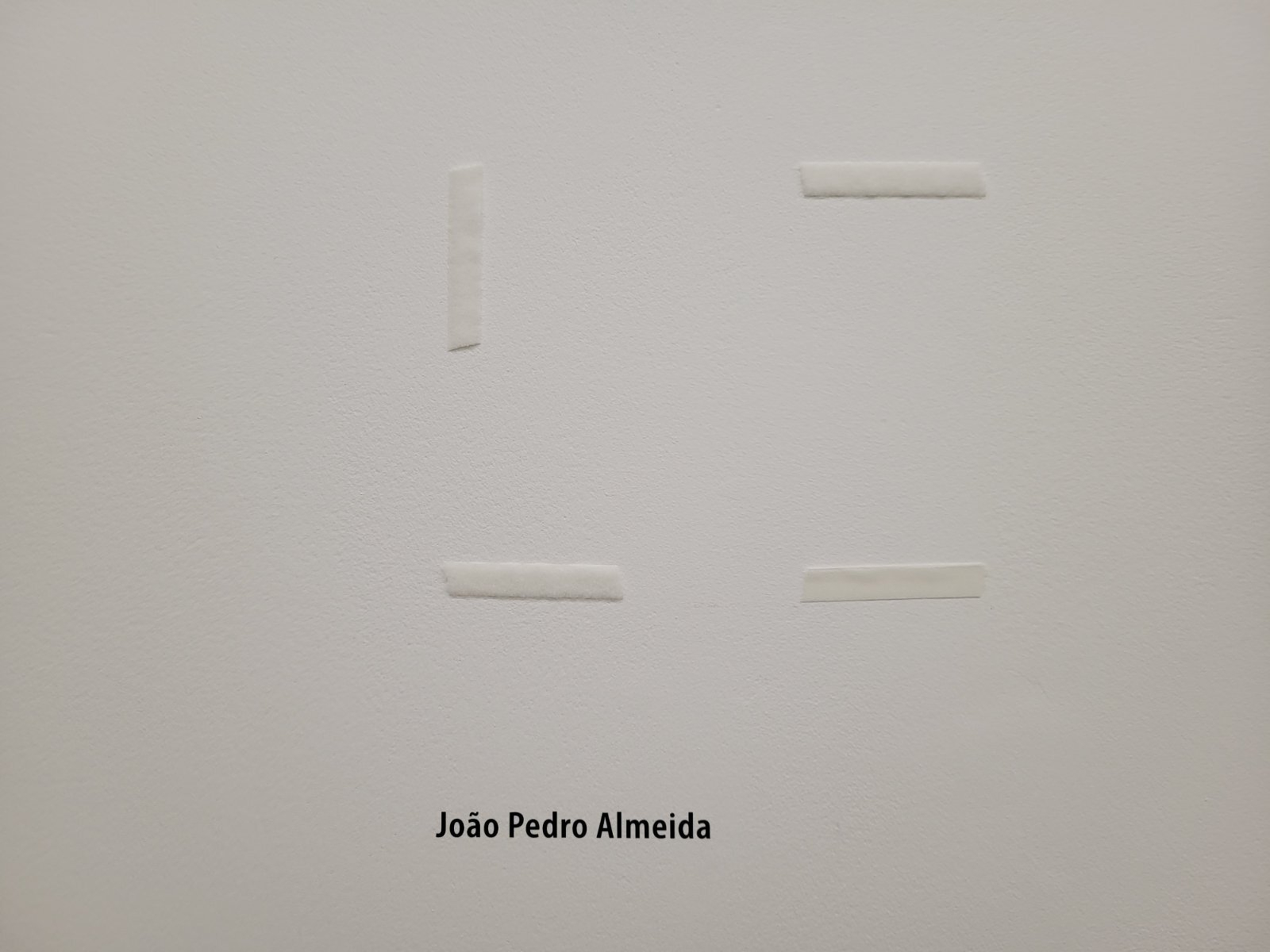 White tape pieces arranged in an abstract geometric shape with the name João Pedro Almeida below.