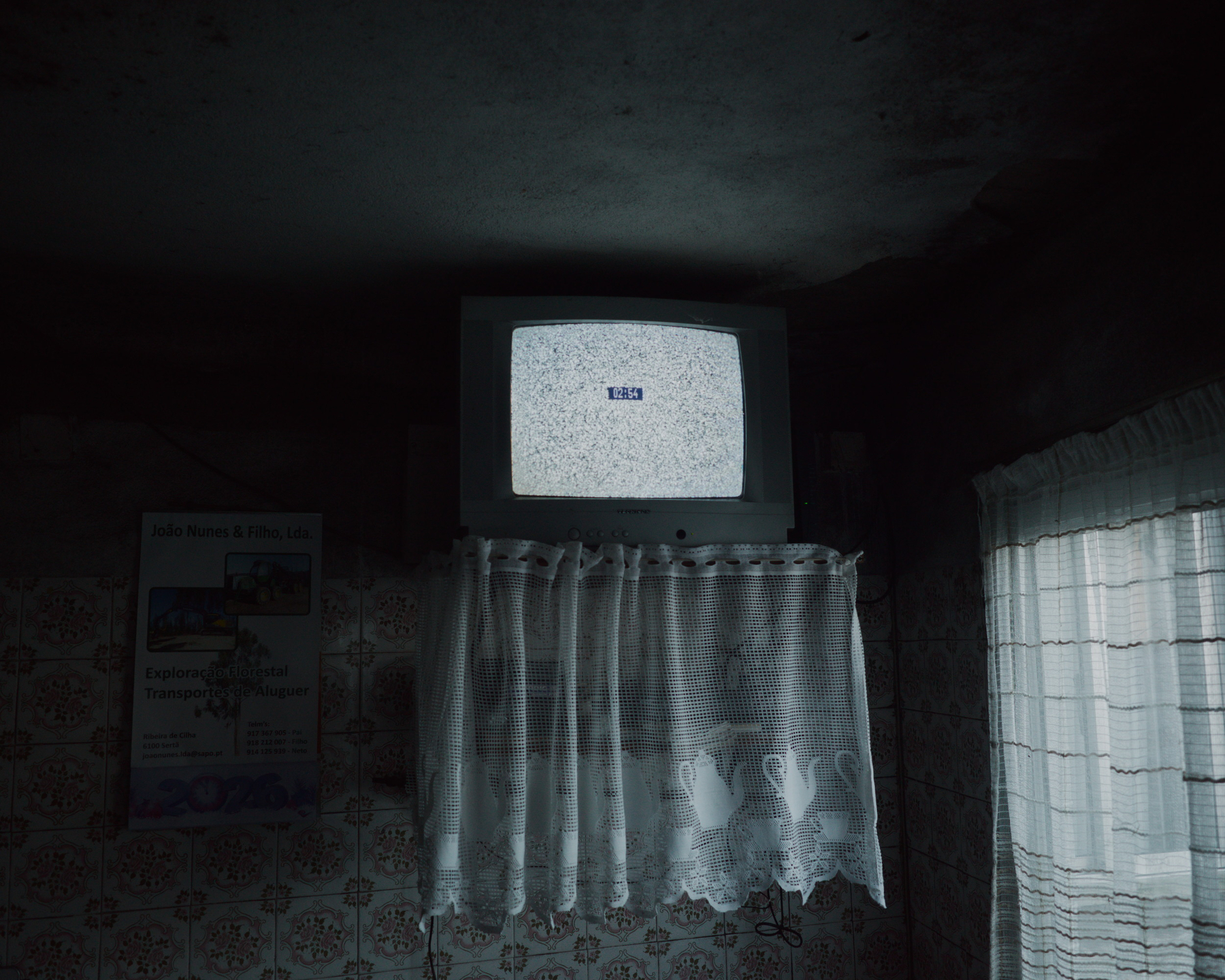 A small television displaying static is mounted above lace curtains in a dimly lit room.