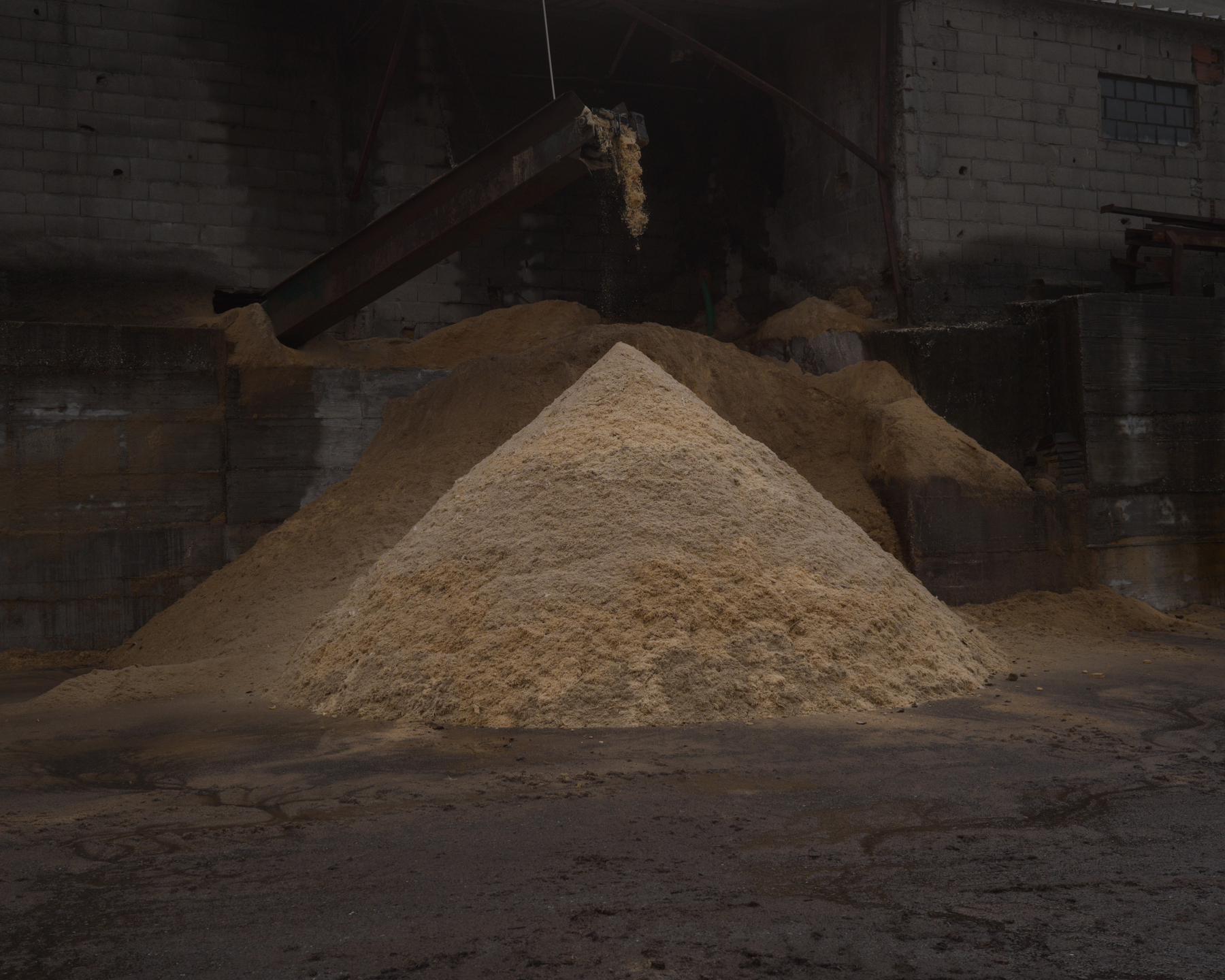 A large pile of sand or sawdust is situated in front of an industrial building.