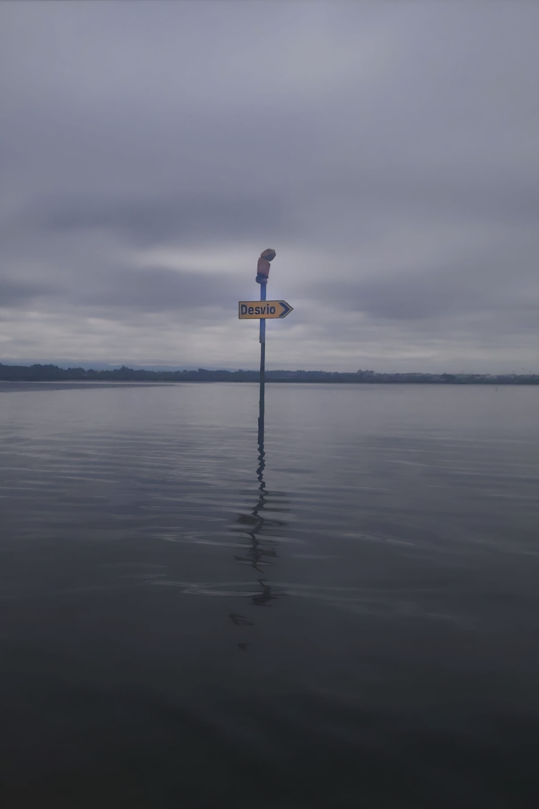 A Desvio sign is partially submerged in calm, overcast waters, suggesting flooding.