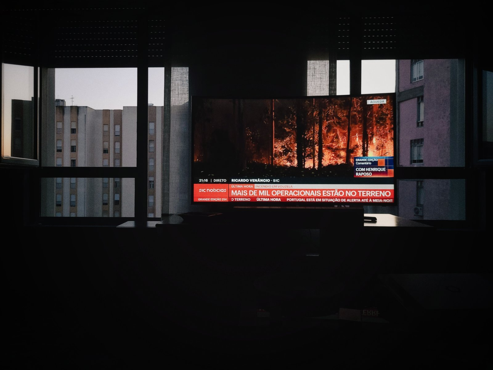 TV showing wildfire, between two windows and with buildings on the background. 