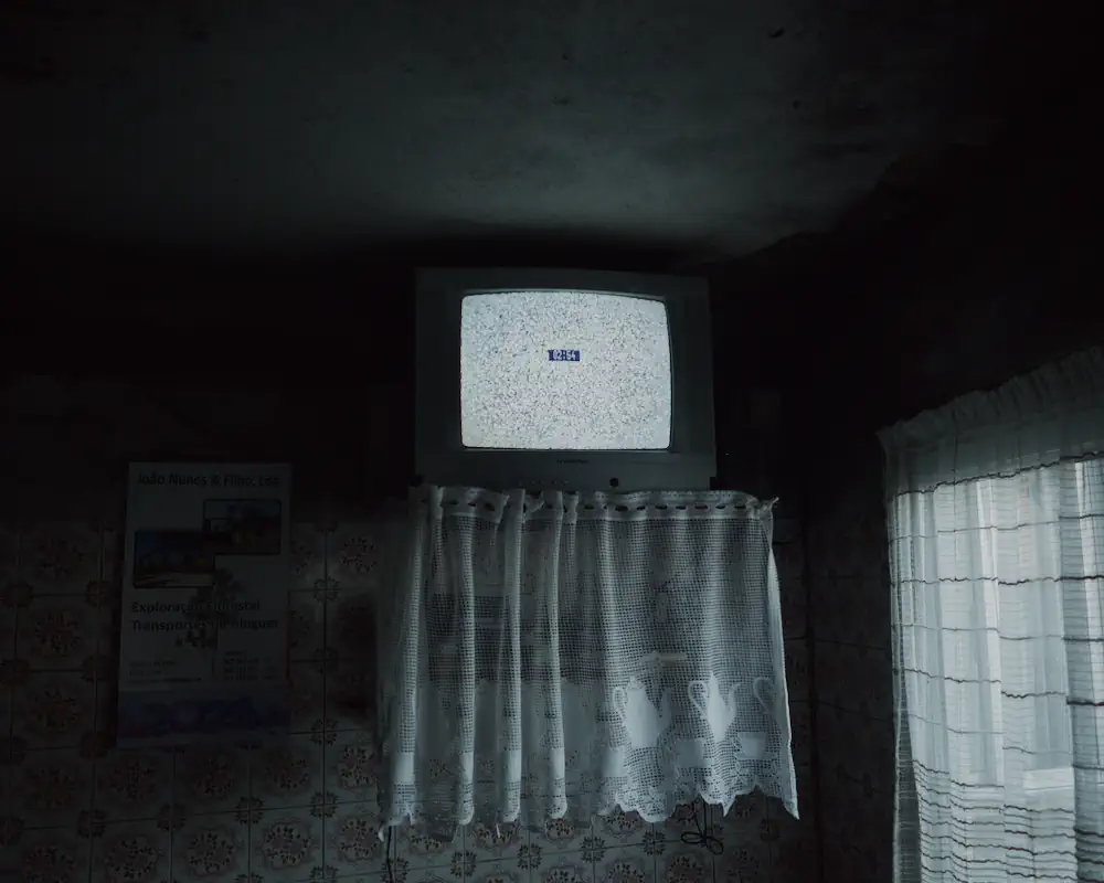 A small television displaying static is placed above lace curtains in a dimly lit room.