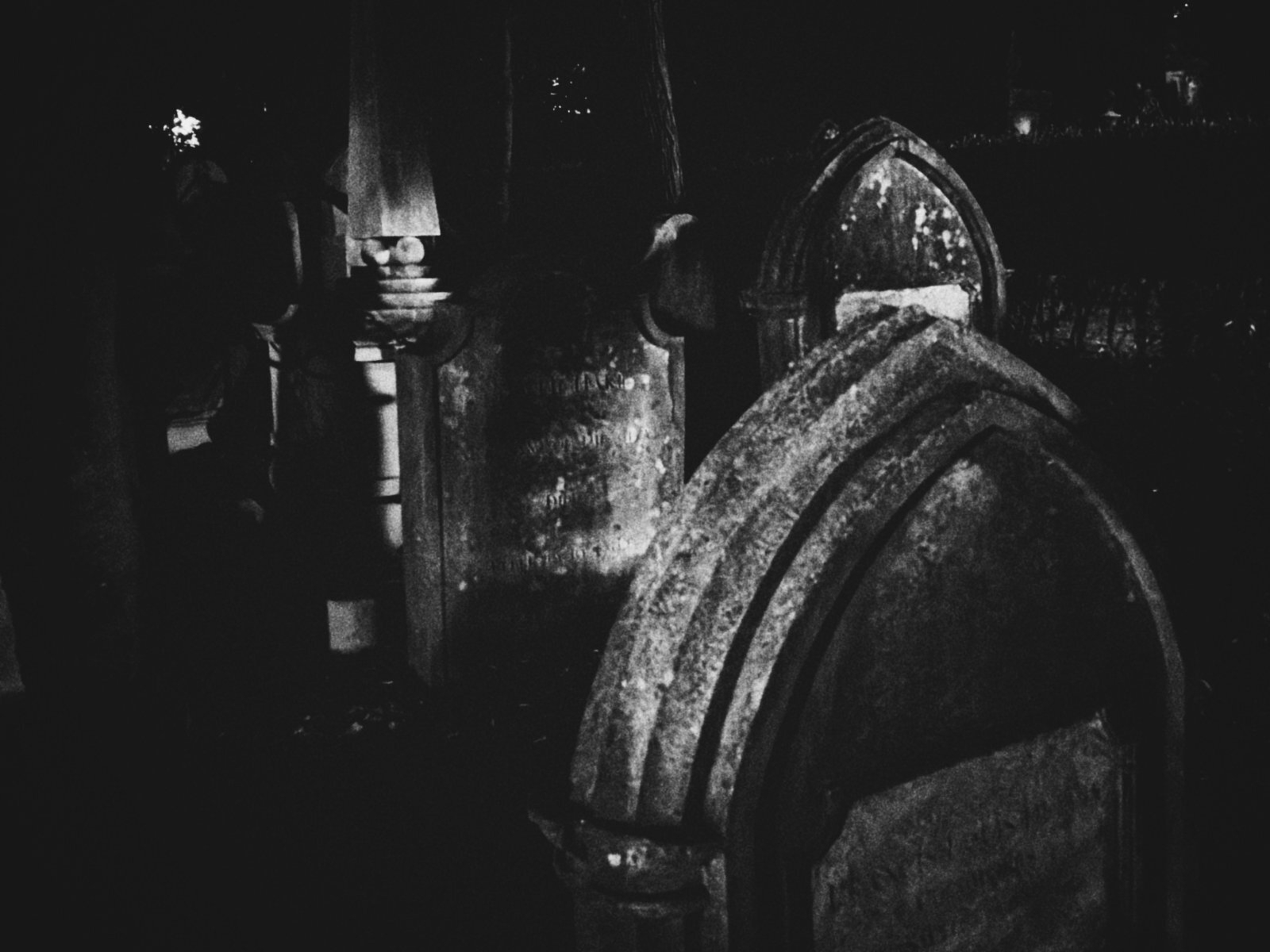 Several old, weathered gravestones are visible in a dark, shadowy cemetery.