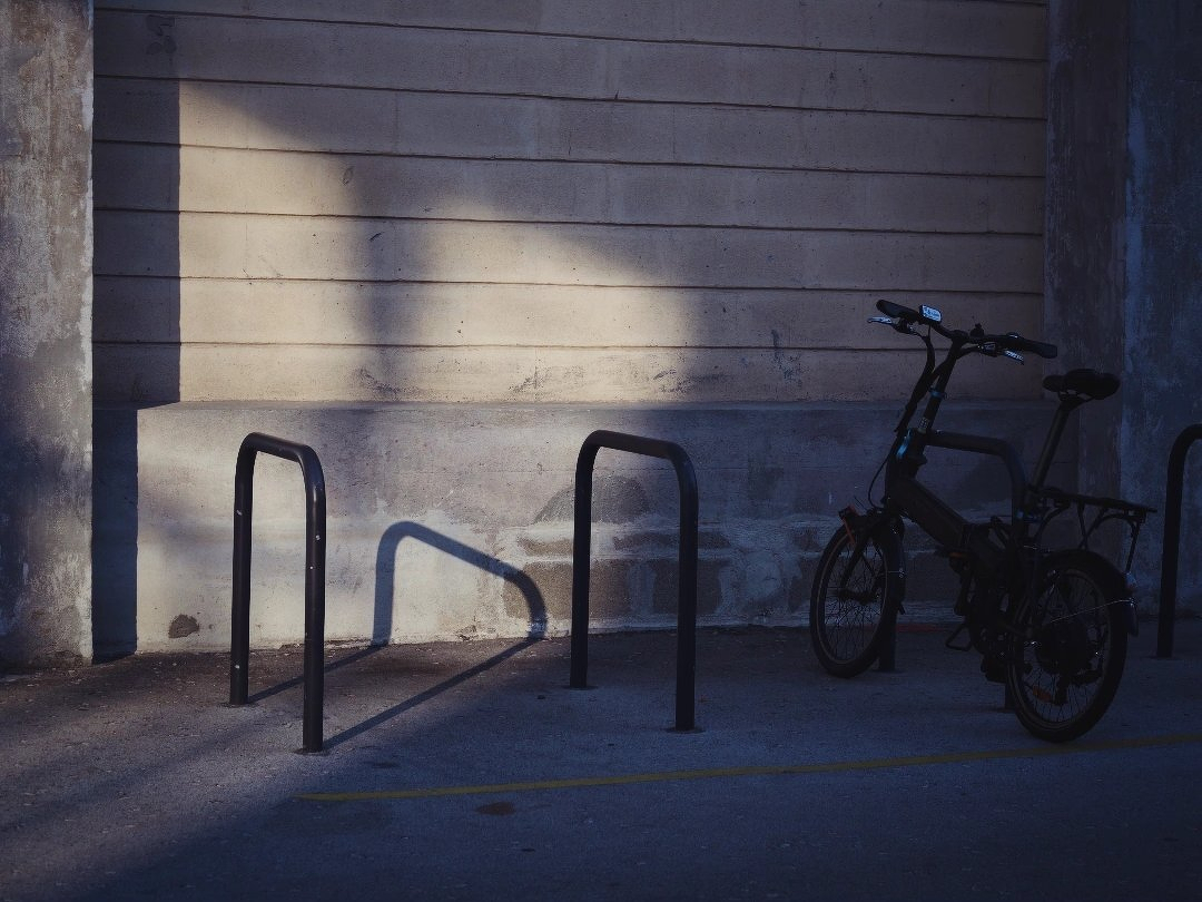 A bicycle is parked next to empty bike racks against a wall illuminated by soft sunlight.