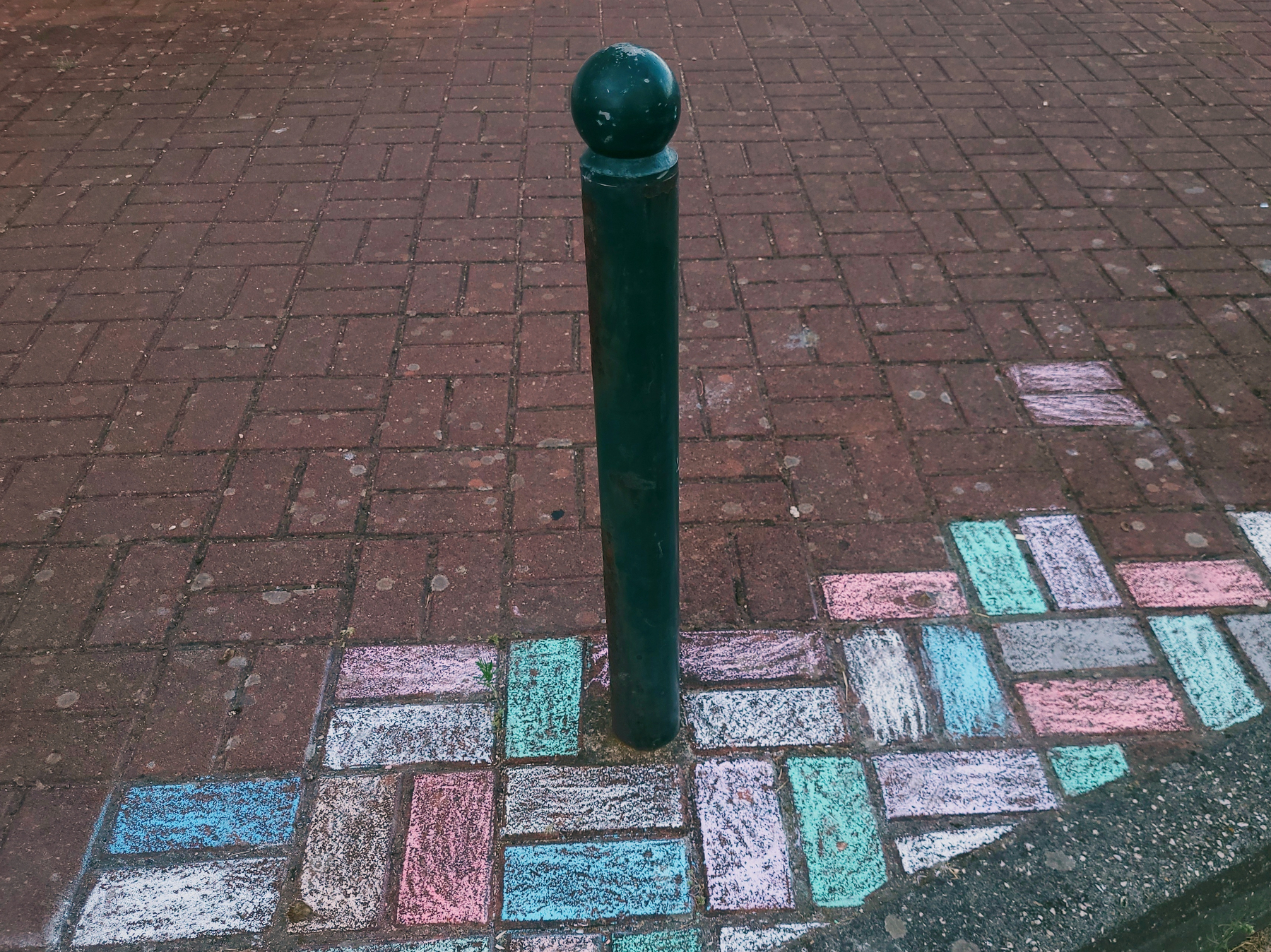 A metal bollard stands on a brick pavement surrounded by colorful chalk-drawn rectangles resembling bricks.